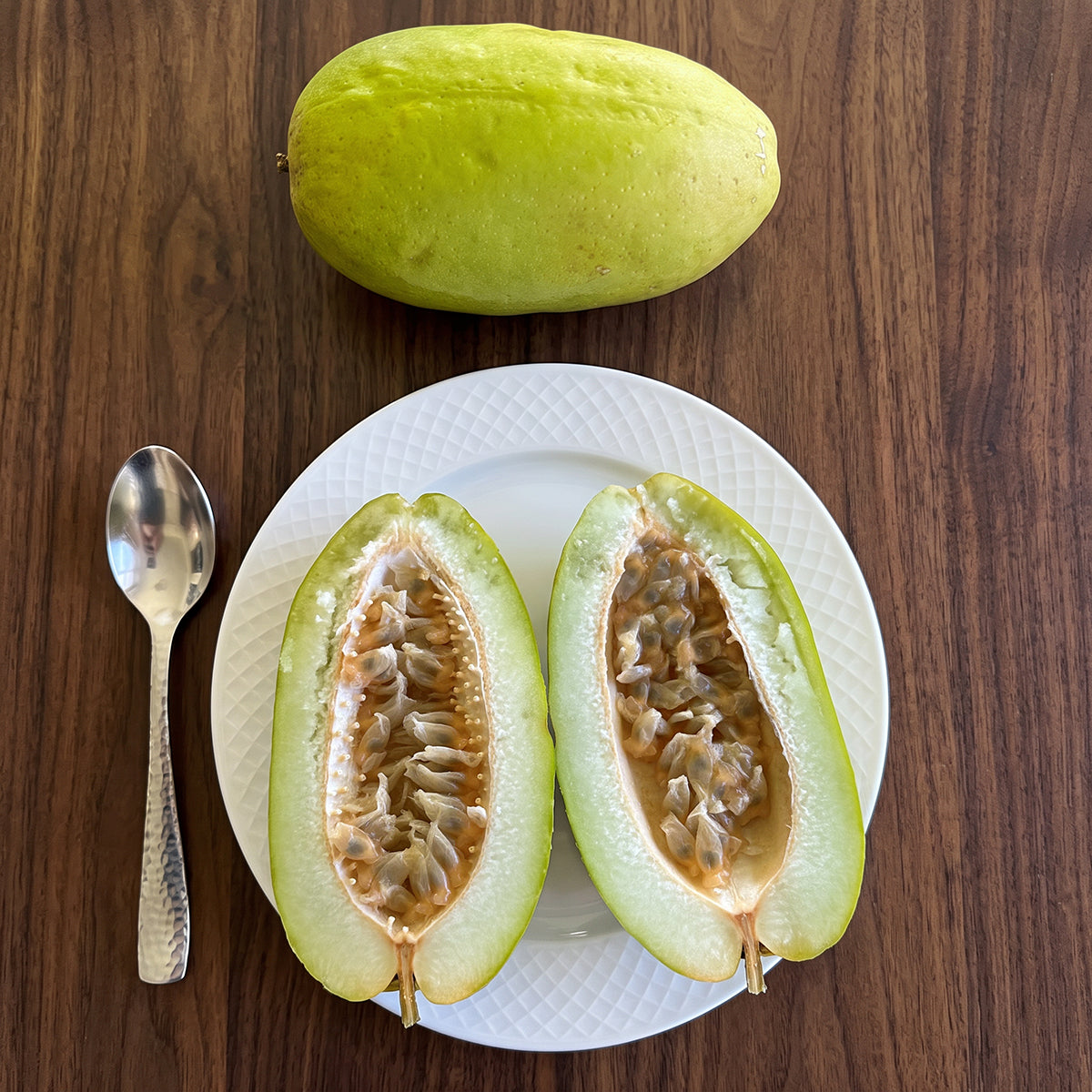 Indian Giant Granadilla Passion Fruit cut open on a plate with a whole fruit above the plate